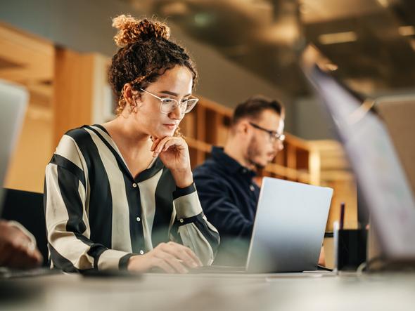 A young woman works intently on a laptop