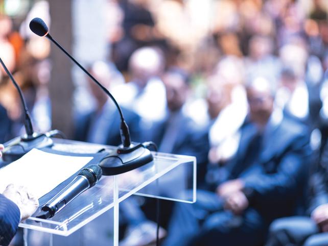 A lectern with two microphones in front of a crowded audience