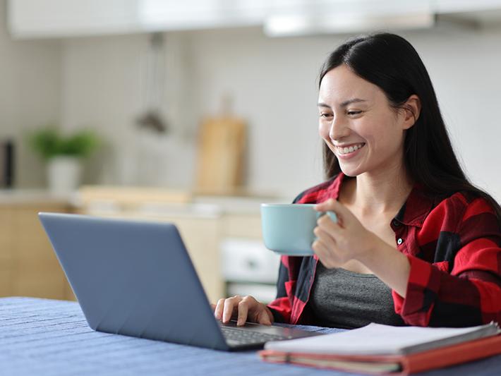 Asian woman drinking coffee at laptop