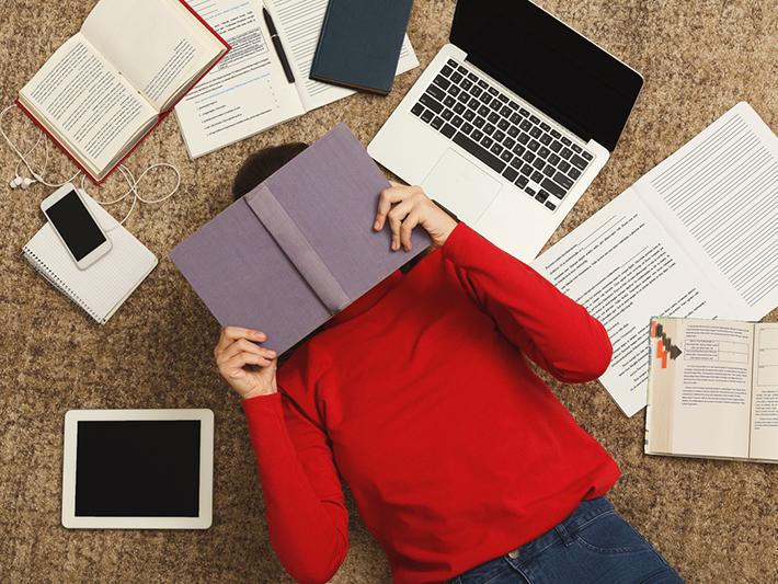 College student hiding face under book, exam stress