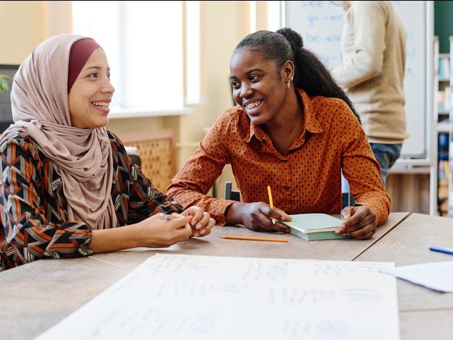 Two women laugh together over a notebook