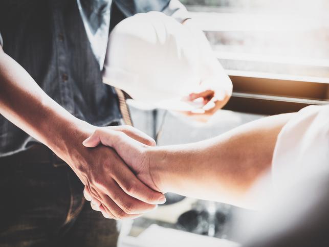 Two people, one carrying a hard hat, shake hands