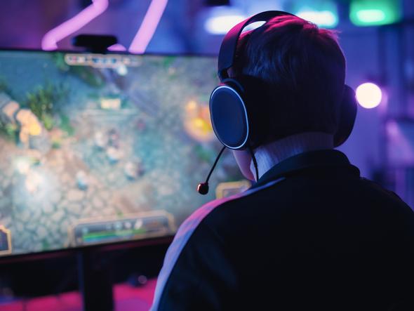 A video gamer with a headset on is seen from the back