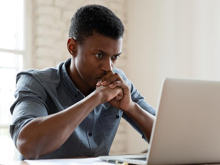 Black male student looking thoughtfully at laptop screen