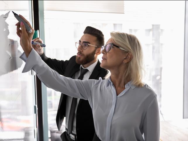Two people write on a whiteboard