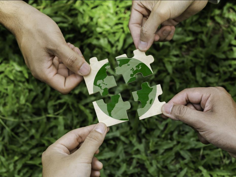 Four hands each with a puzzle piece that together makes up an image of the planet