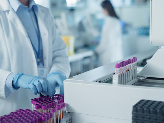 A white-coated figure handles test tubes