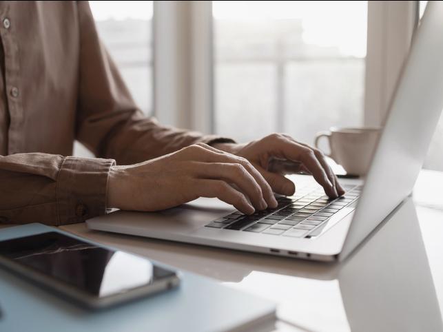 A man types on a laptop, smartphone in the foreground
