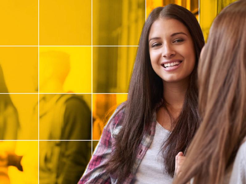 Young female student speaks to a friend while holding textbooks