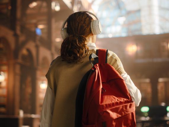 A student walks into a library, wearing headphones