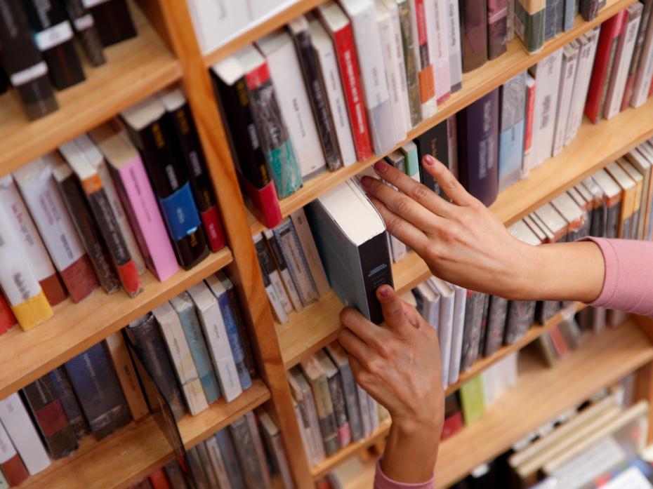 A hand taking a book out of a shelf in a library