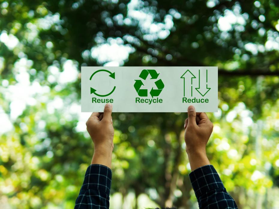 Hands holding up a sign that says "reuse", "recycle" and "reduce" with accompanying icons