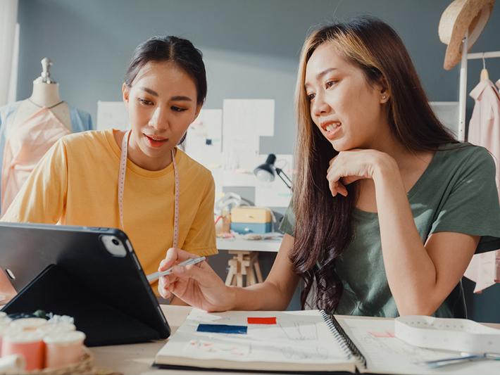Two female Asian fashion design students in workshop