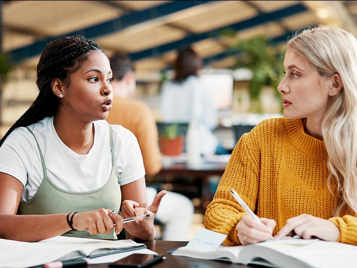 Two young female college students talking in library