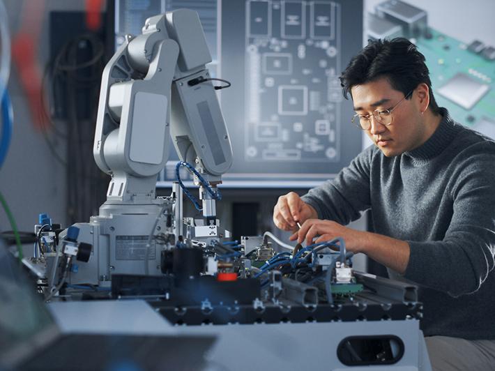Male Asian student working on a robot arm