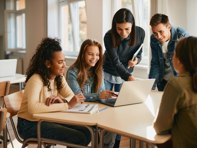 Students and support staff work together round a laptop
