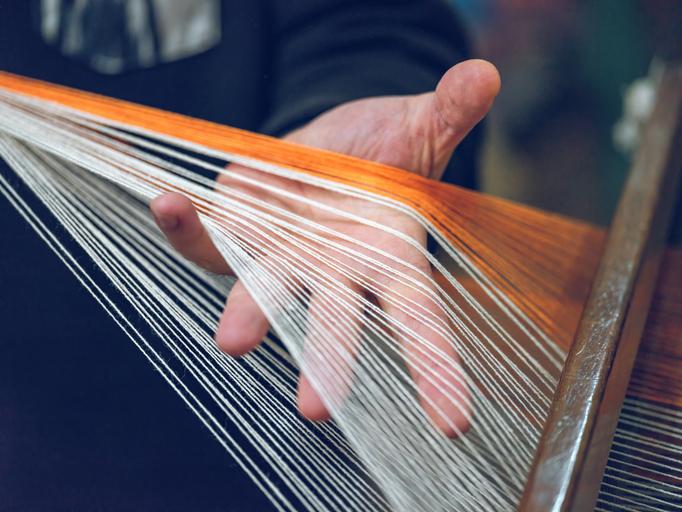 A hand weaves fabric on a loom