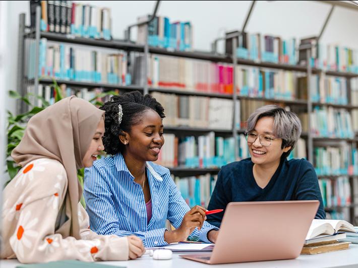 Three female students in library around laptop