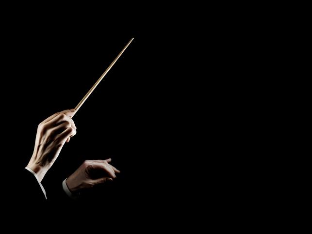 A conductor gestures with a baton against a black blackground