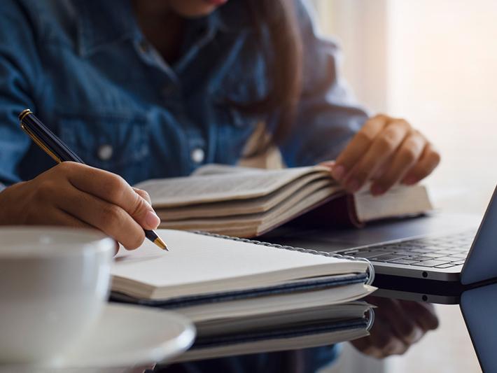 Young woman writing notes with a pad and laptop
