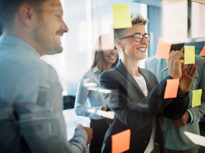 Colleagues looking at sticky notes on glass wall