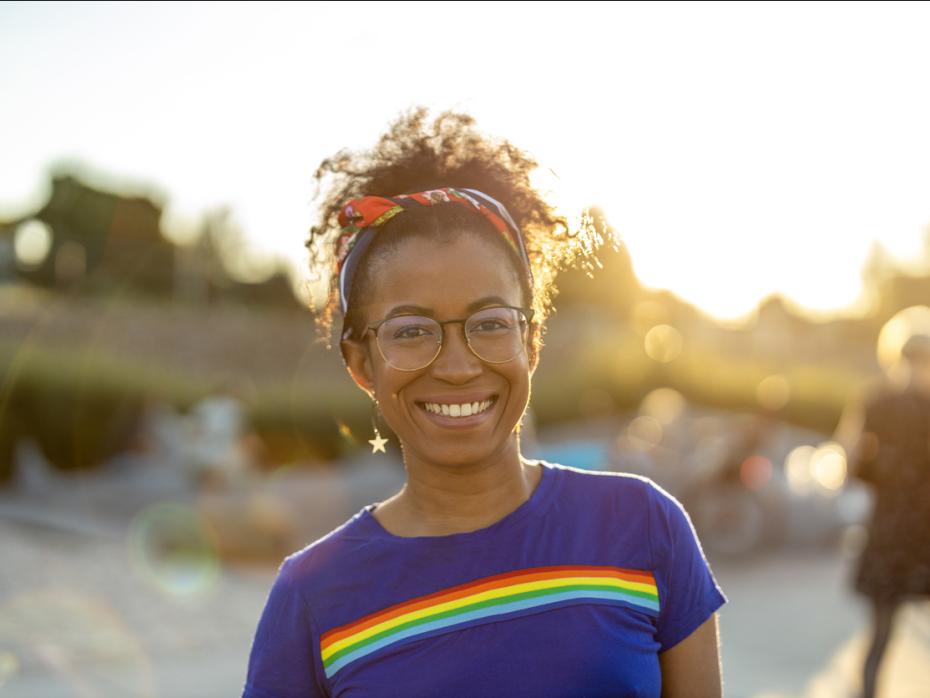 A young woman smiling to camera ourside wearing a t-shirt with a rainbow on it