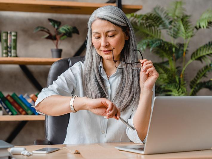 Mature Asian woman looking at watch with laptop
