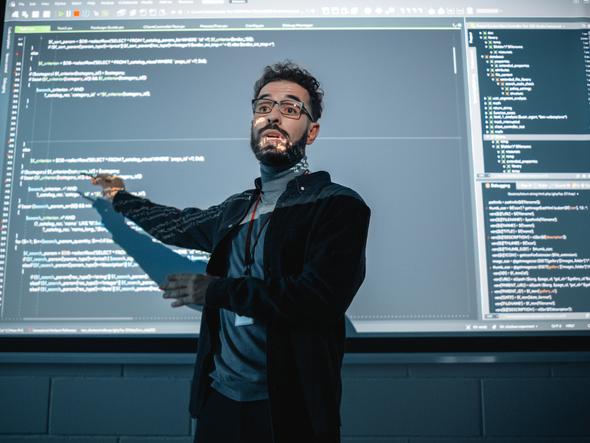 A teacher stands in front of a projector screen