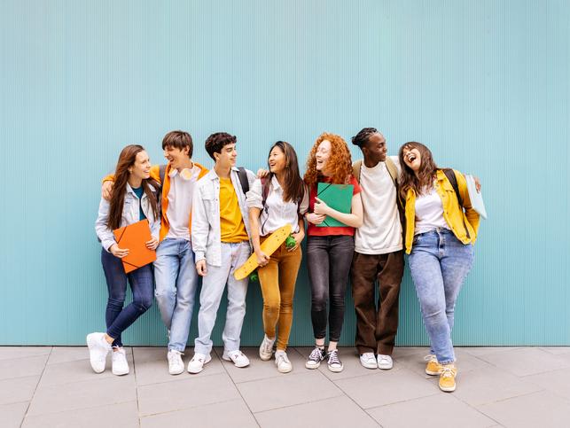 Students laugh together in front of a blue wall