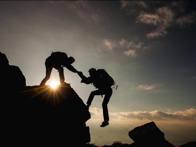 One mountain climber helps another over a ridge