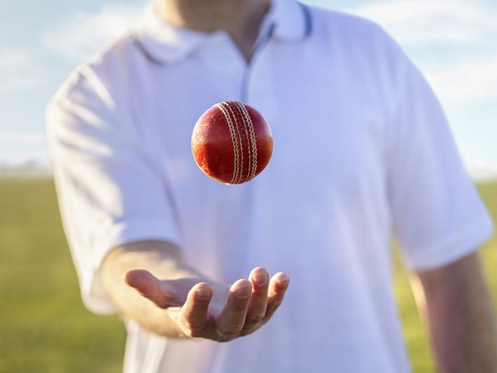 Cricket player tossing ball in hand on pitch