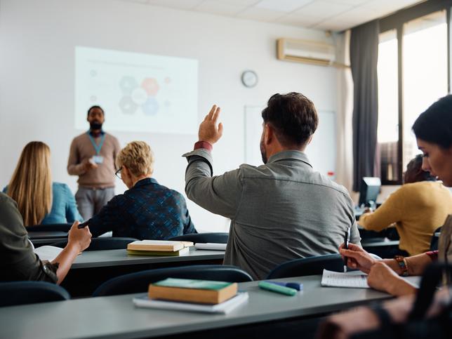 Back view of student raising his hand to answer teacher's question