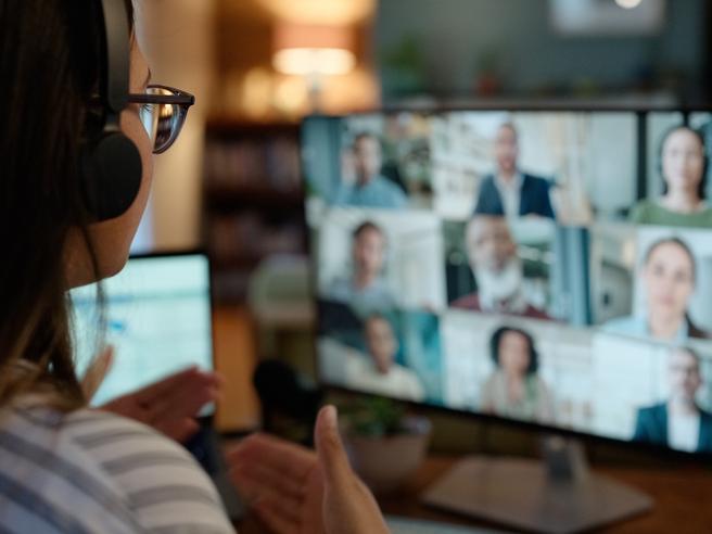 A student wearing headphones speaking to a screen with other students online