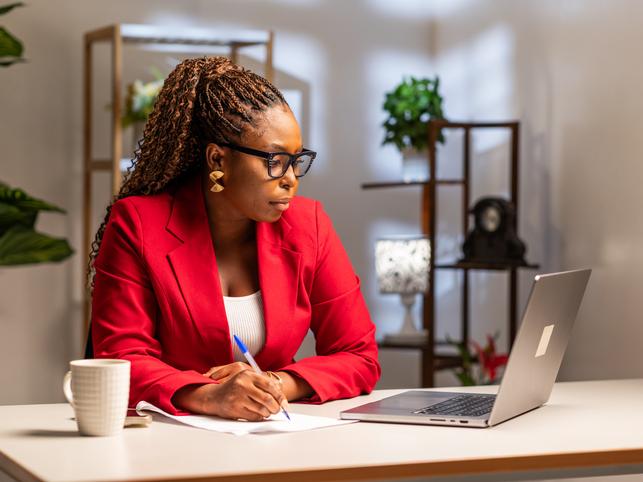 A Black female academic with glasses sat at a desk on her laptop