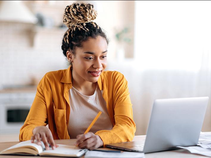 Black female student taking notes at laptop