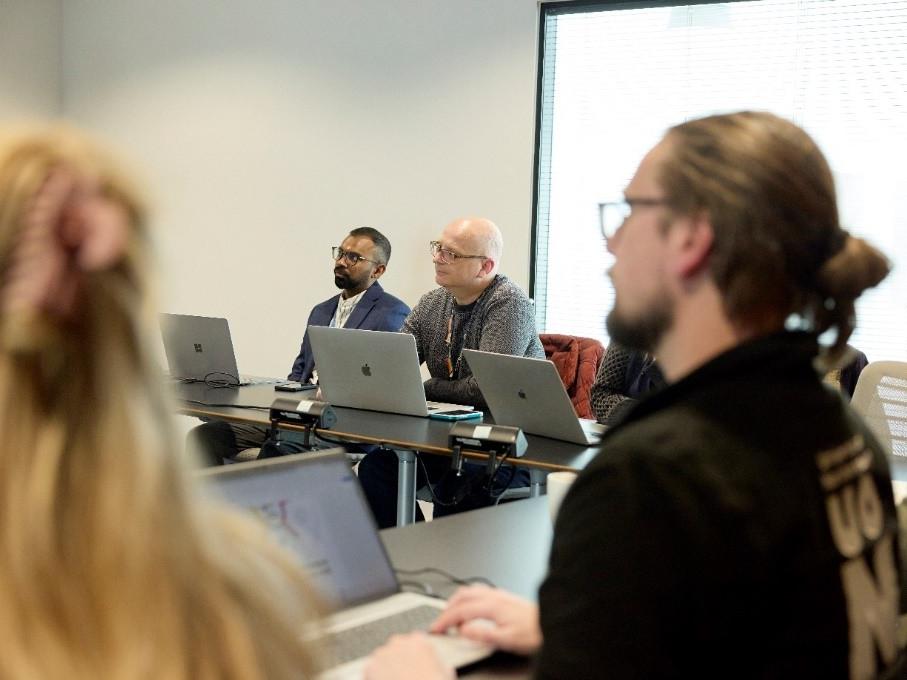 University staff on laptops listening to a speaker out of shot