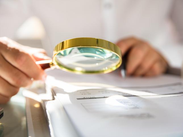 A hand holding a magnifying glass over a stack of papers