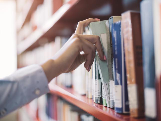 A hand pulling out a book from a library shelf
