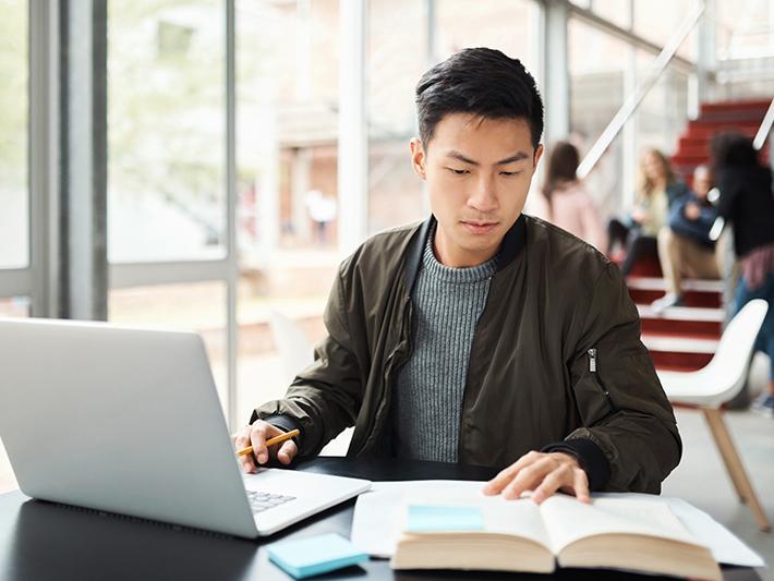 Male Asian student writing on laptop in common area