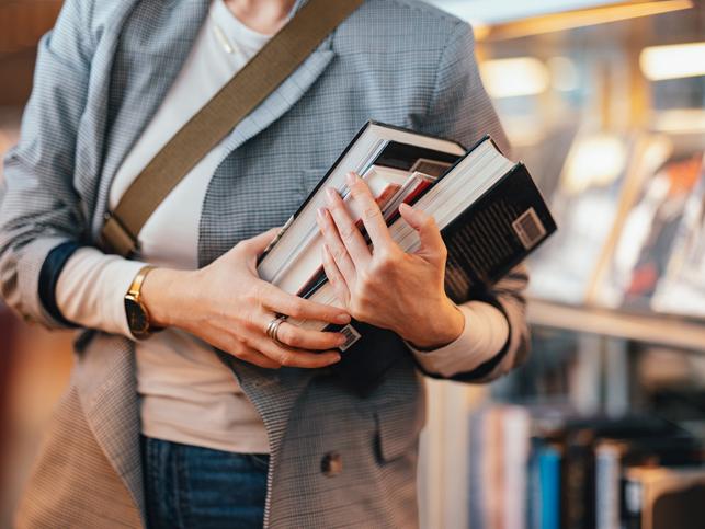 A woman holds a pile of books 
