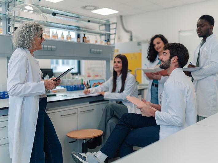 Diverse group of young adult students listening to their mature female professor during a chemistry lecture in a lab