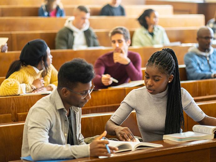 Two students in lecture hall look at a book