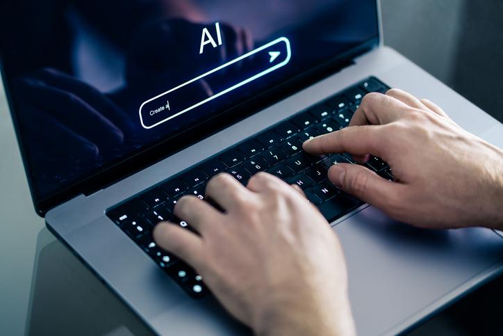 Hands type on a laptop with "AI" on the screen
