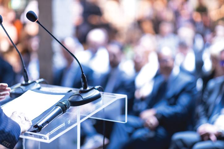 A lectern with two microphones in front of a crowded audience