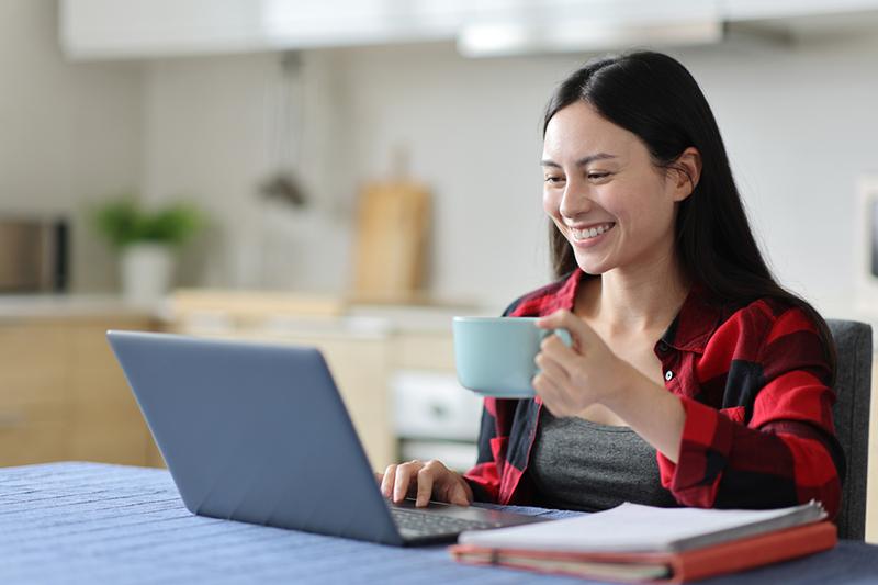 Asian woman drinking coffee at laptop