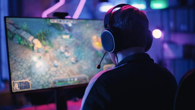 A video gamer with a headset on is seen from the back