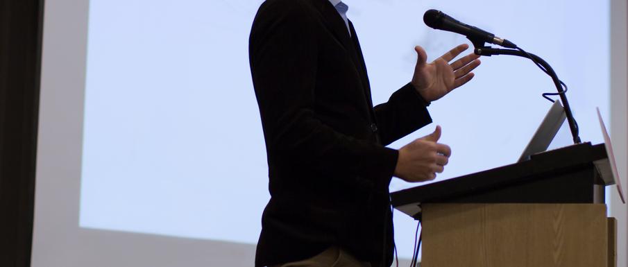 A lecturer stands in front of a microphone
