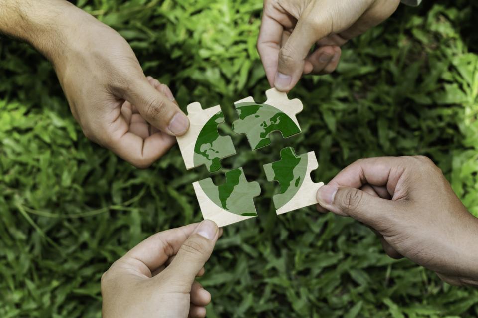 Four hands each with a puzzle piece that together makes up an image of the planet