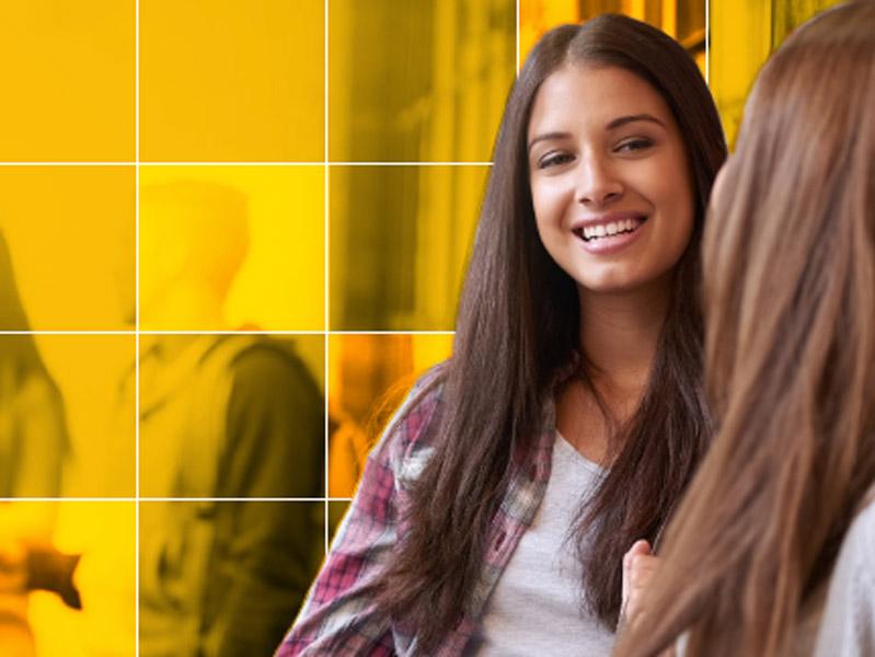 Young female student speaks to a friend while holding textbooks