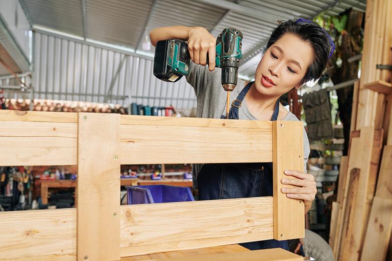 Young woman with a drill assembling a wooden bookcase